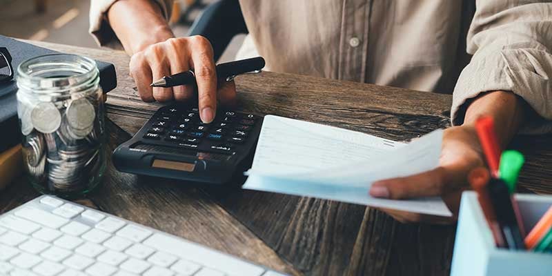 Person using a calculator and reviewing paperwork at a wooden desk